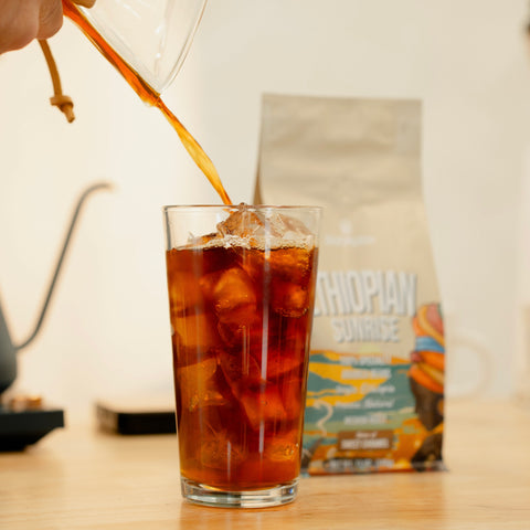 Glass of iced coffee with a straw, blurred coffee package in the background