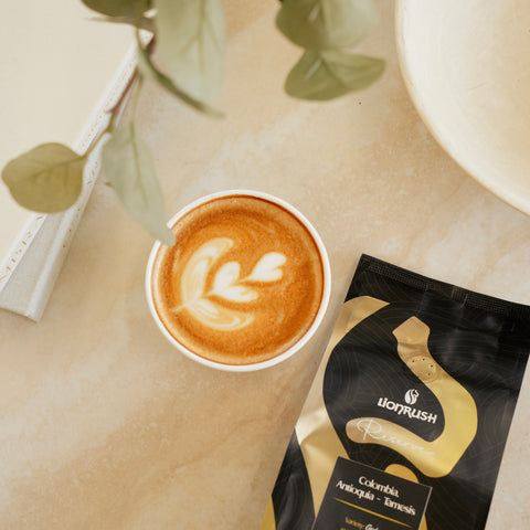 Cup of coffee with latte art next to a bag of Lionrush coffee reserve on a light surface.